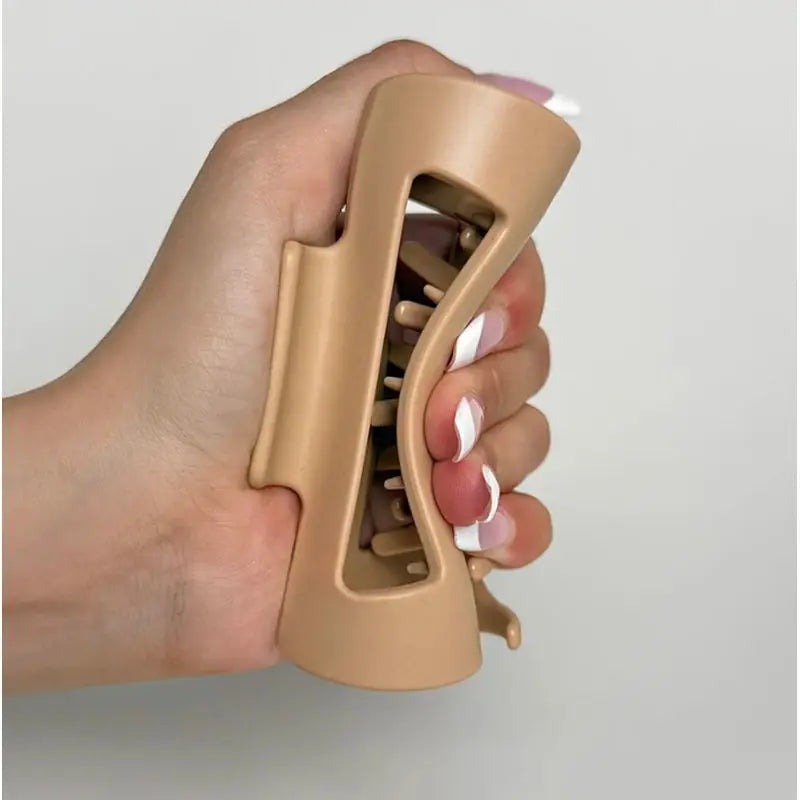 Hand holding a beige  silicone claw clip  against a plain background