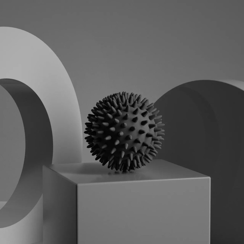 Black textured  Spiky massage fascia ball  on a gray pedestal with abstract shapes in the background