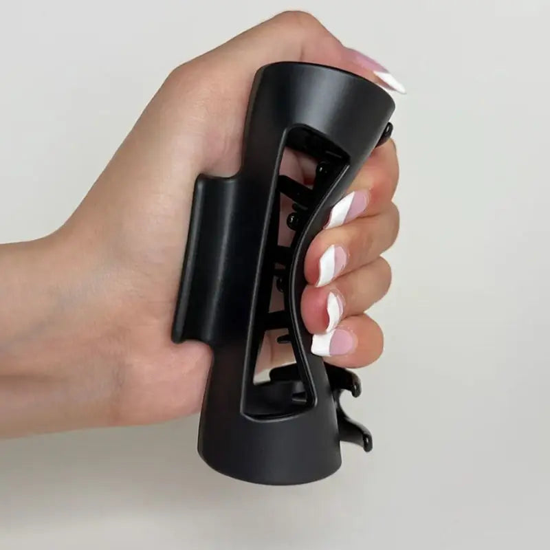 Hand holding a black silicone claw clip against a plain background
