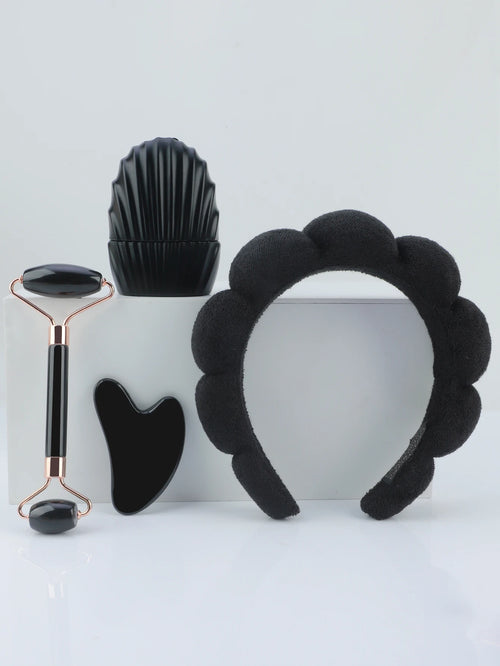 Set of black facial tools including a roller, gua sha tool, and headband on a light gray background