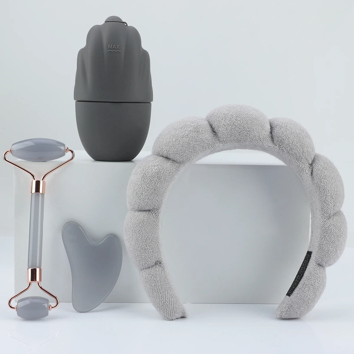 Set of skincare tools including a gray roller, face ice roller and headband on a light gray background