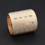 Decorative cylindrical hair roller with textured surface and gold rim on a black background