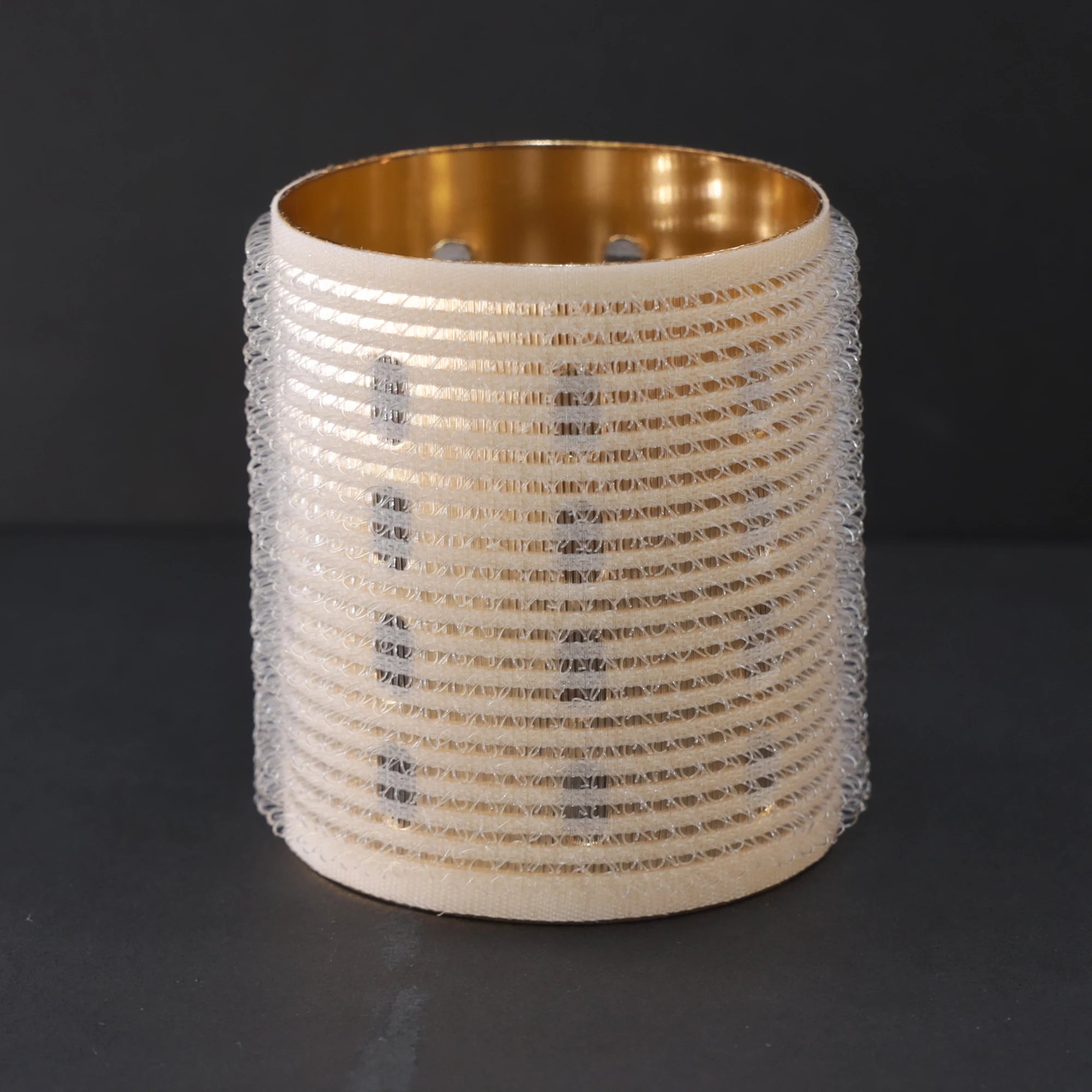 Decorative hair roller with gold interior and textured exterior on a black background