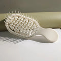 White hairbrush on a light surface with a neutral background. Mini Travel Hair Brush 
