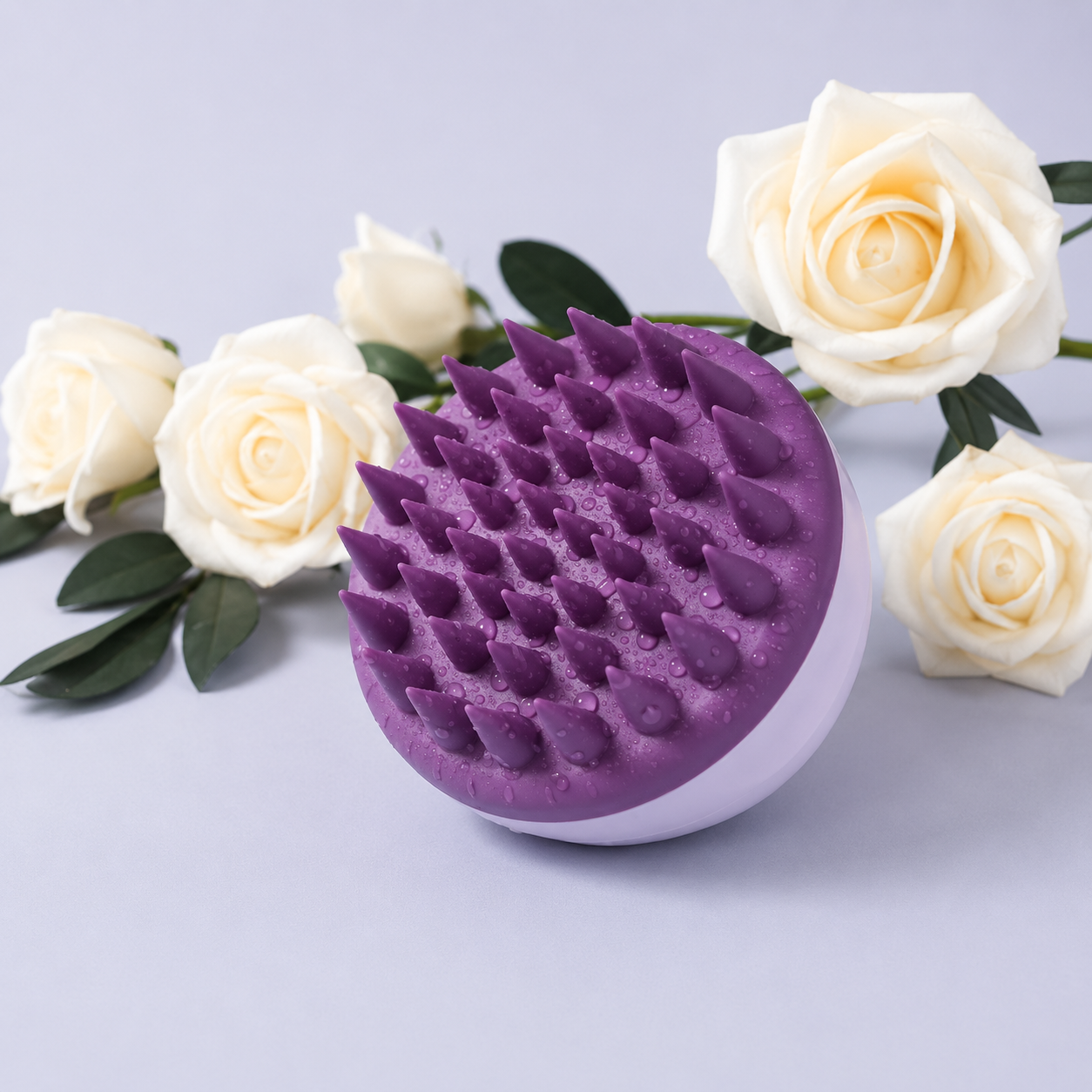 A purple and white scalp massage brush with textured silicone nubs, styled with white roses on a light gray background.