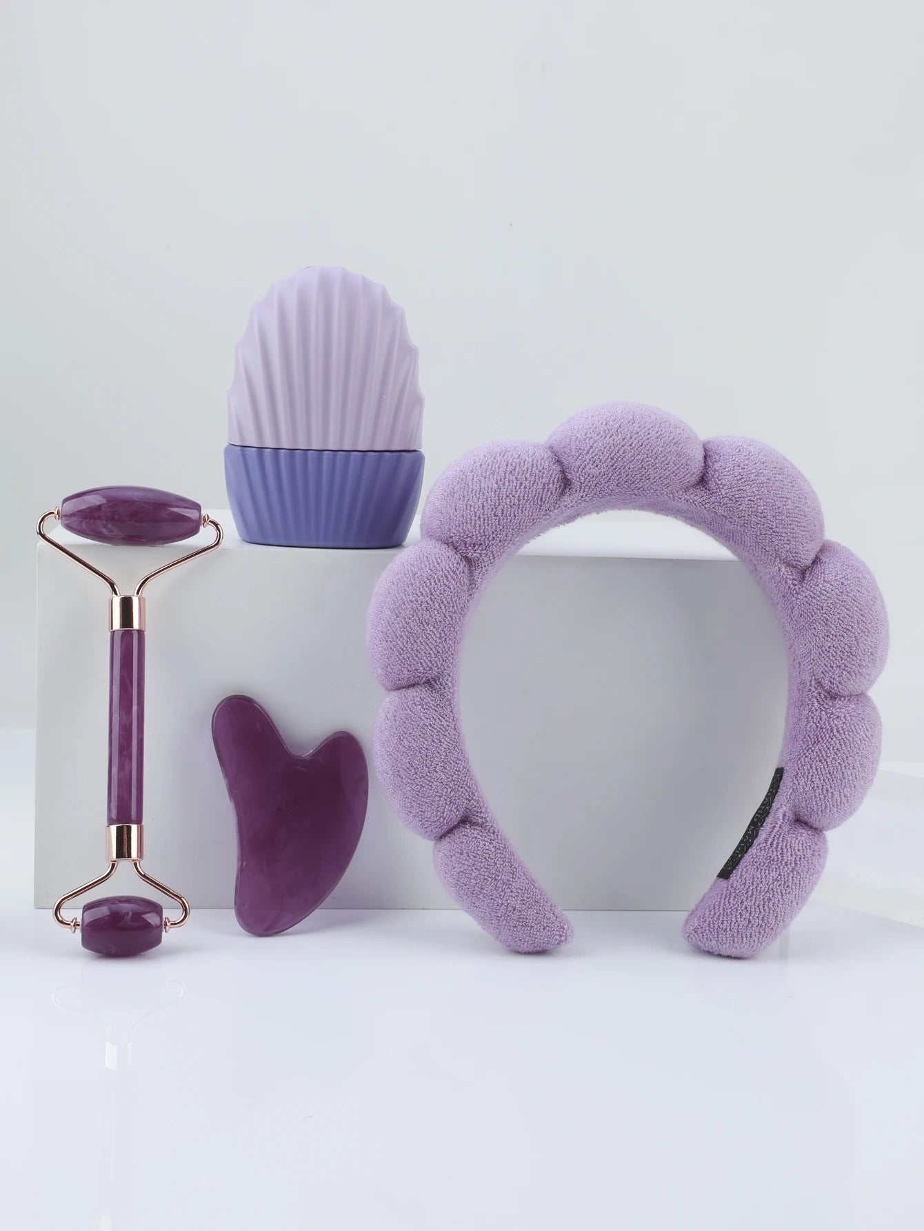 Set of purple skincare tools including a ice roller, roller, face mask, and headband on a white background