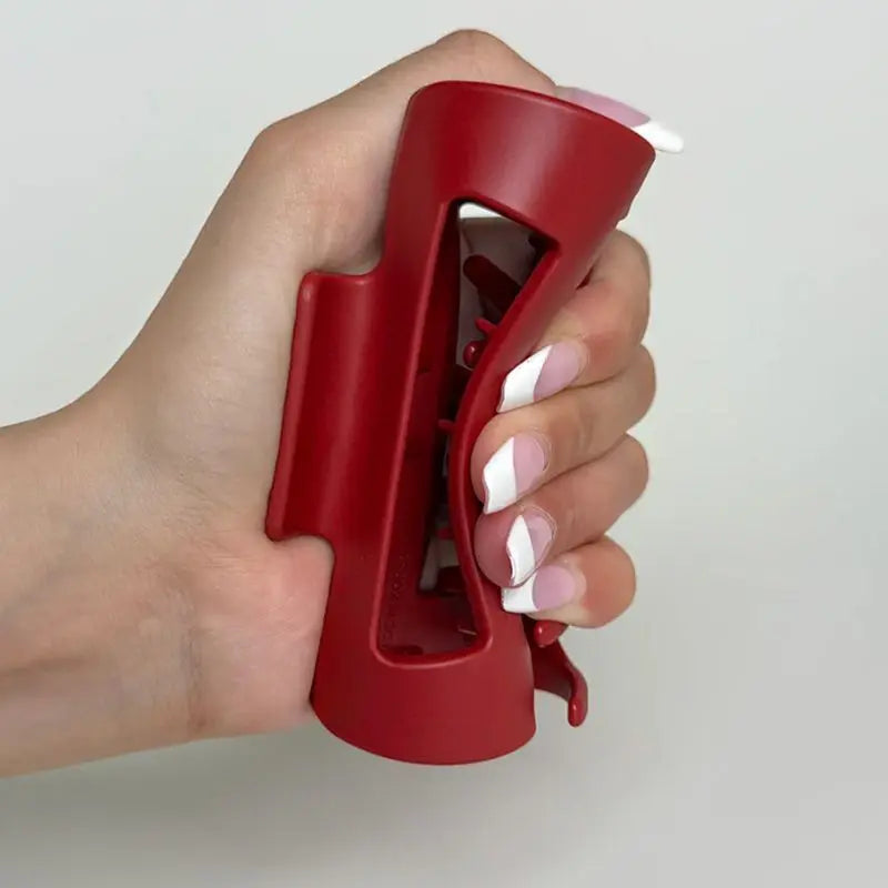 Hand holding a red silicone claw clip against a plain background