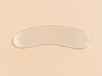 A clear, silicone curved gel pad or eye patch lying horizontally on a solid, warm beige background.