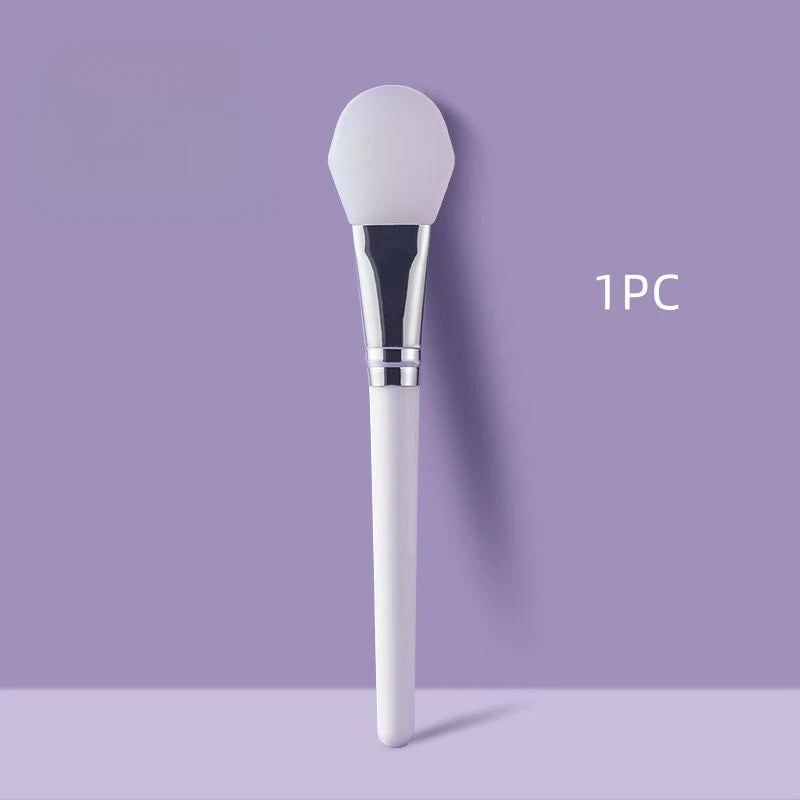 Face mask brush with white bristle silicone head and silver handle on a purple background