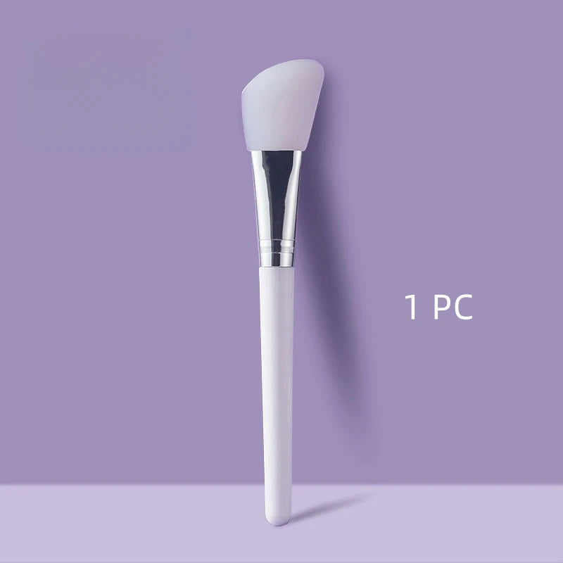 Face mask brush with white handle and silicone attachment on a purple background