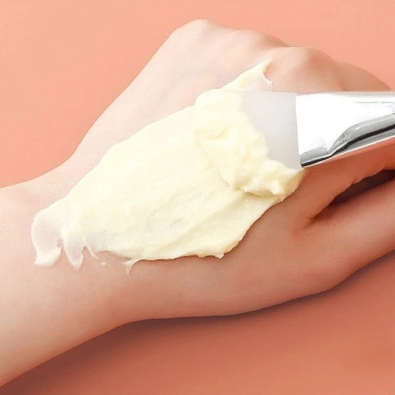 Hand applying a white cream to another hand against a peach background