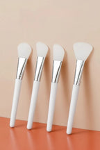 Four silicone mask brushes with white handles on a peach background