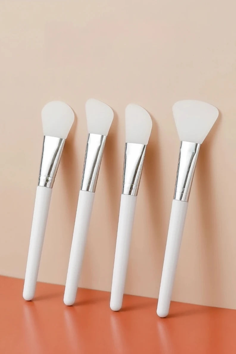 Four silicone mask brushes with white handles on a peach background
